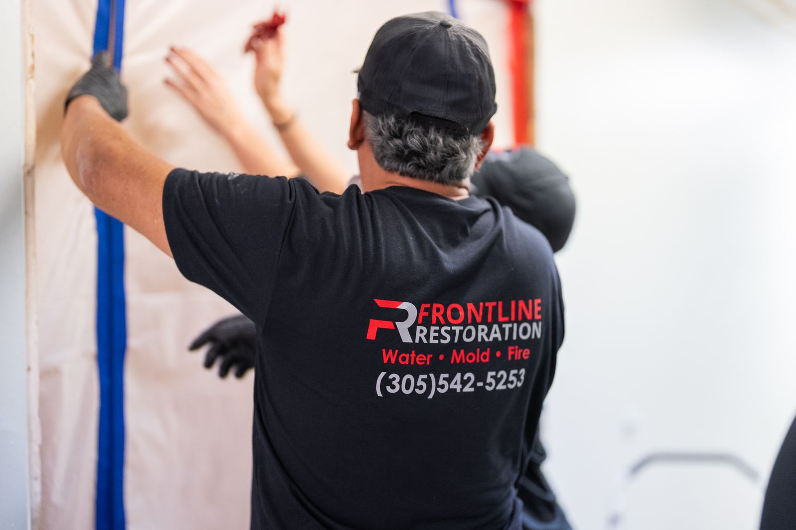 Technician taping plastic containment sheeting to a wall